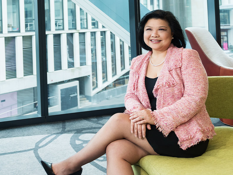 A business woman sitting in a modern office in a pink blazer and smiling. Macquarie - Margaret