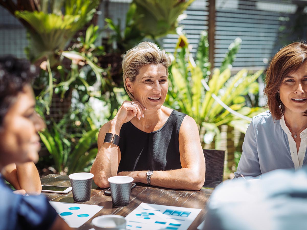 Group of professionals having a business meeting in outdoor cafe or restaurant where they discuss the investment ideas and cooperation plans while drinking coffee. Group of businesswomen and businessmen enjoying working together