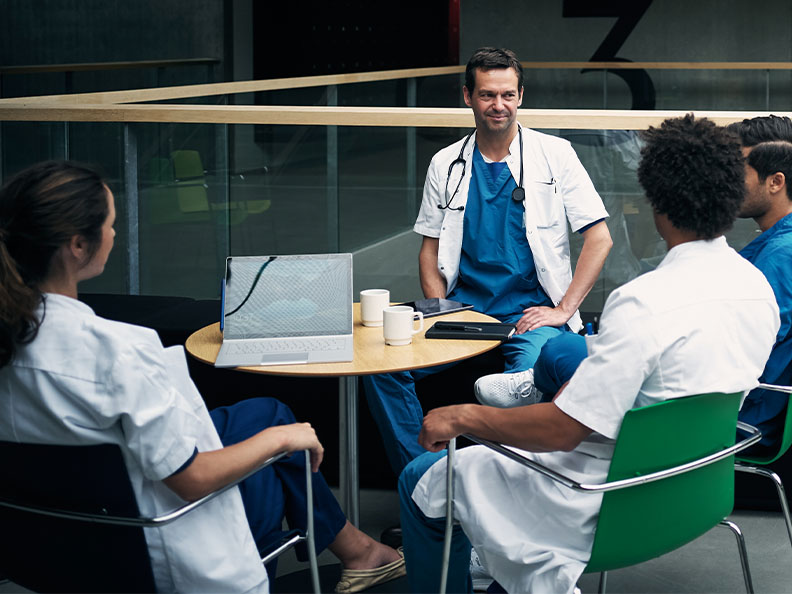 Shot of a group of medical staff seated around a table drinking coffee and having a discussion inside a hospital