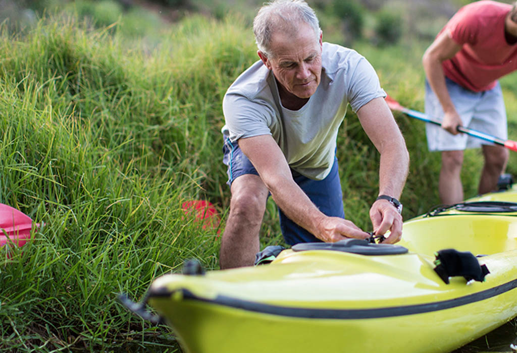 Elderly man rigging up a kayak with a friend