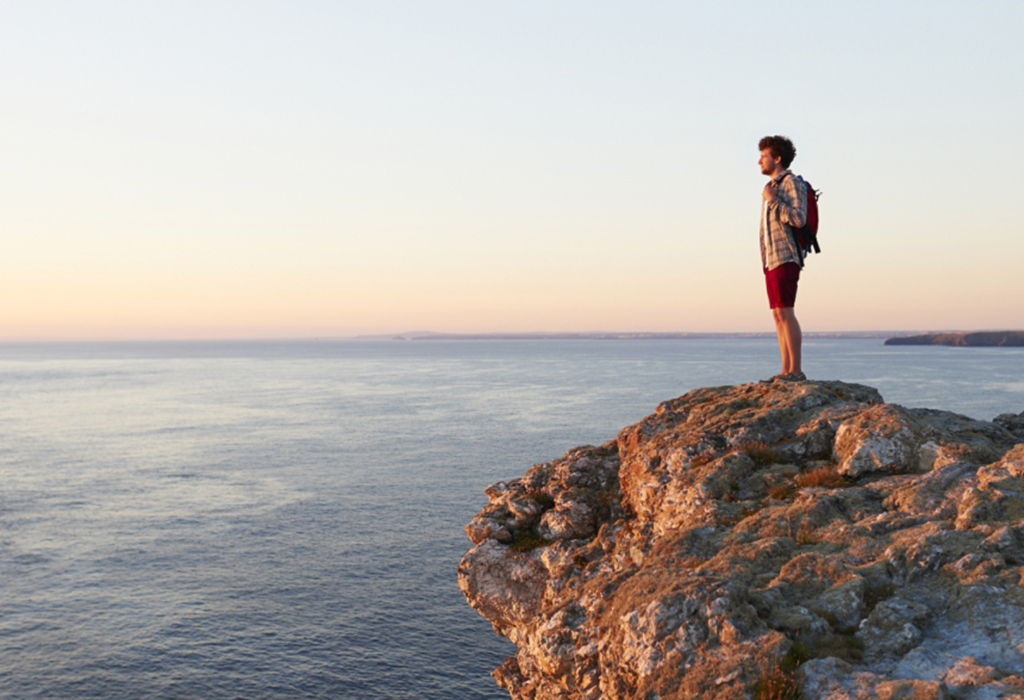 man with backpack looking out to ocean on cliff