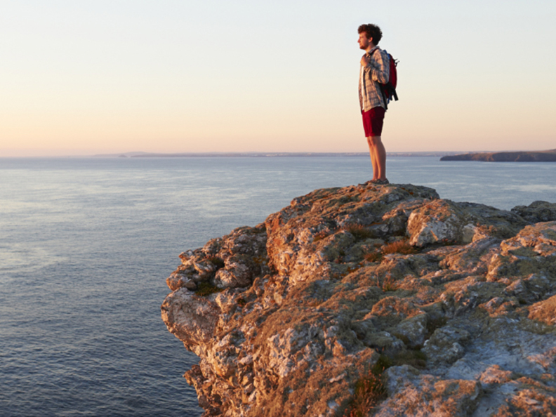 man with backpack looking out to ocean on cliff