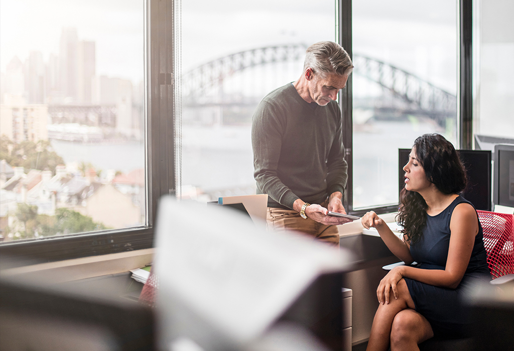 Two coworkers chatting over paperwork with Sydney Harbour Bridge in the background