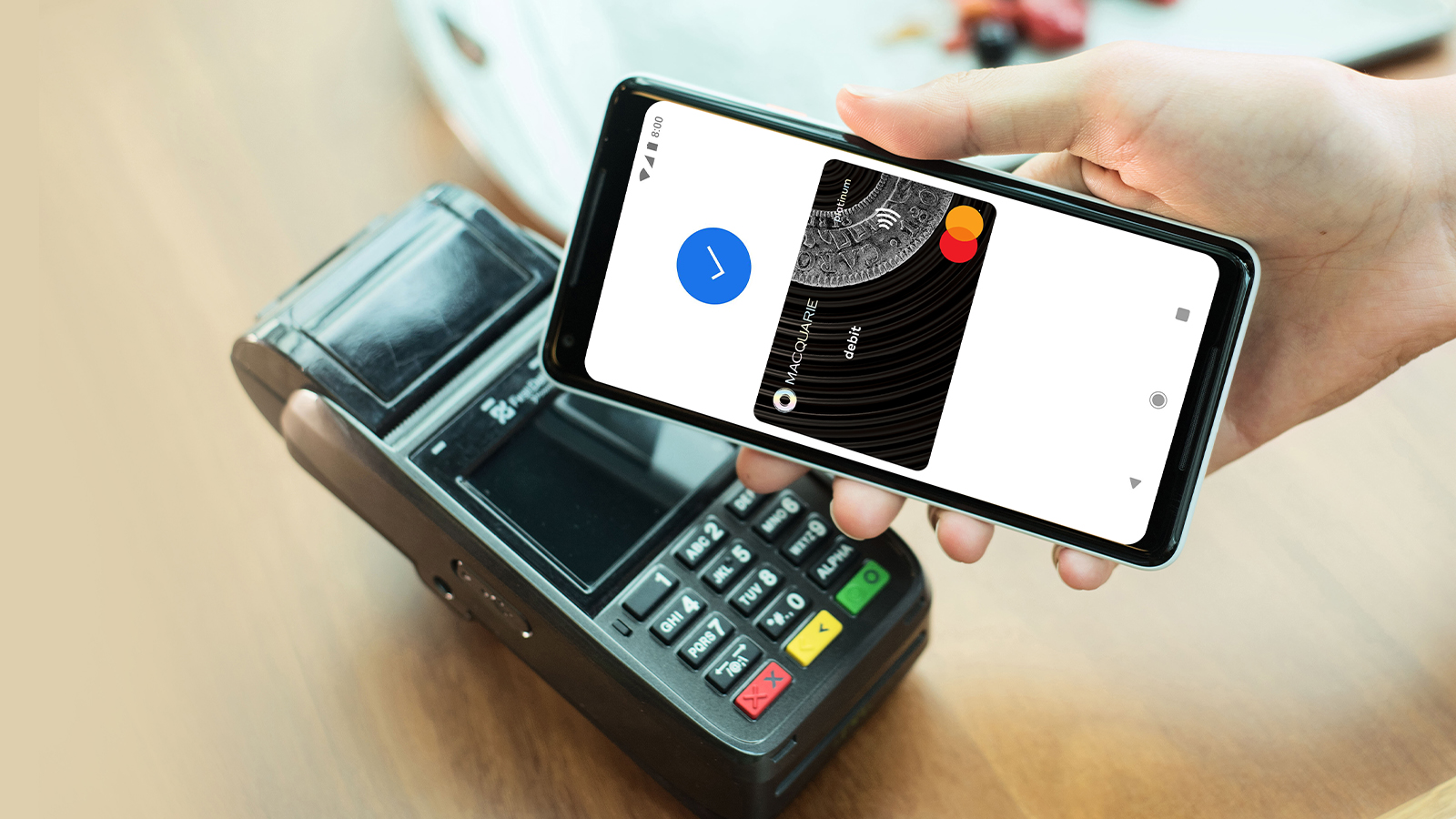 Hand holding a phone over an eftpos machine showing a successful transaction using a Macquarie card with Google Pay