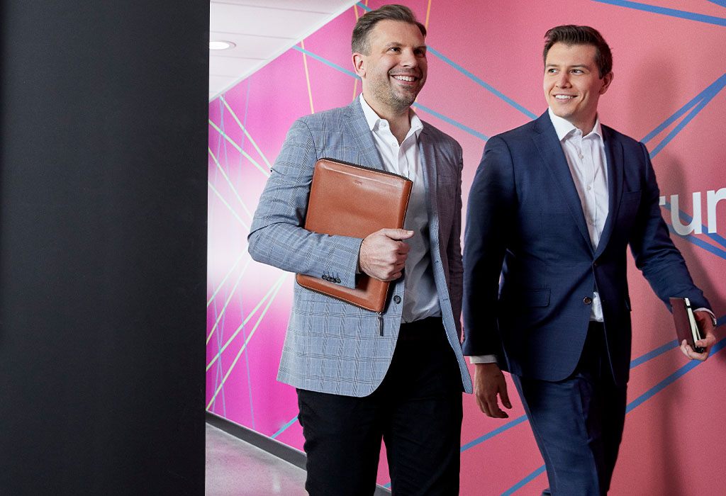 Two men in suits walking down a corridor with a colourful wall behind them. Macquarie customer - ReadyTech