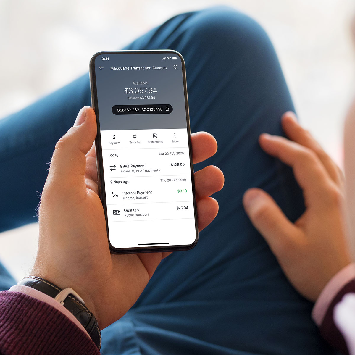 A man lounging back and using his smart phone with the Macquarie bank app open on a transactions screen