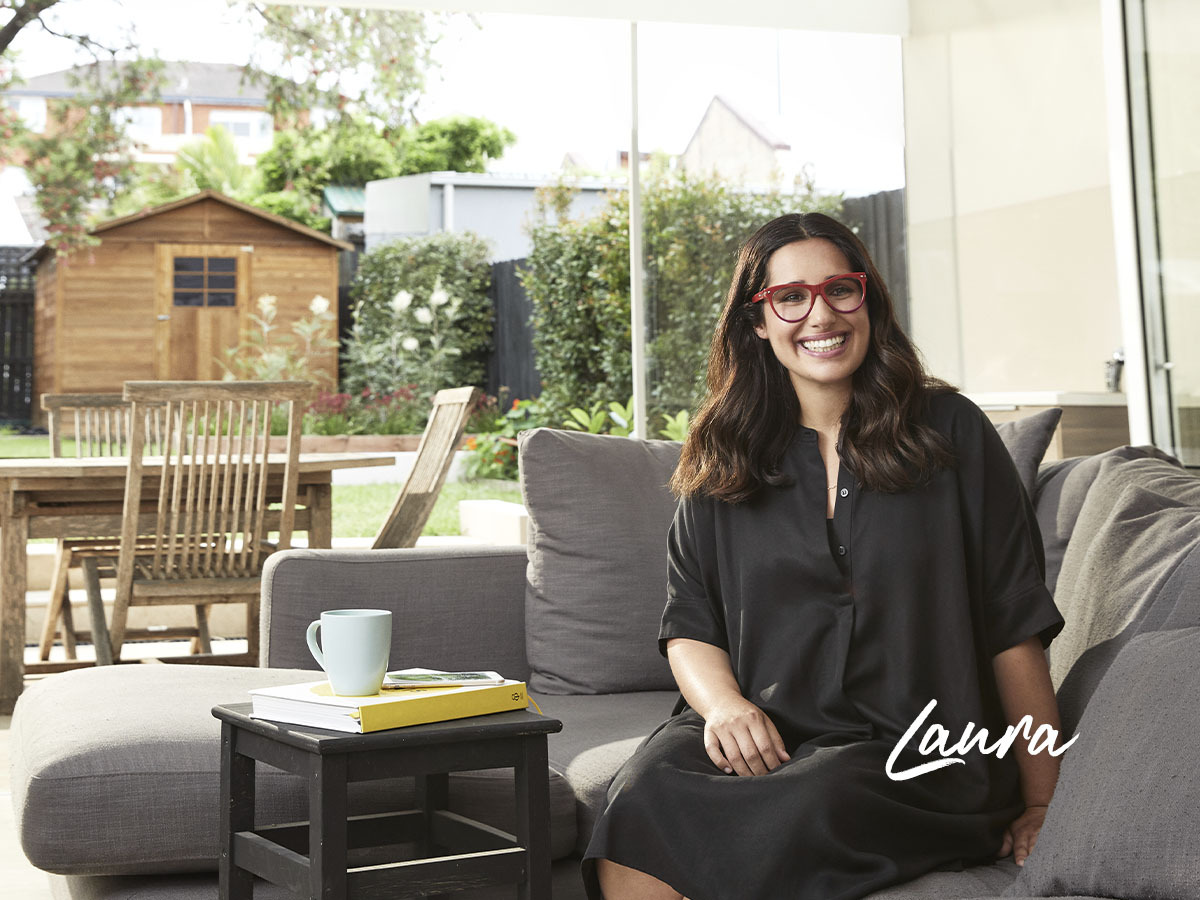 Laura Bates home loan customer with red glasses sitting on couch in house smiling