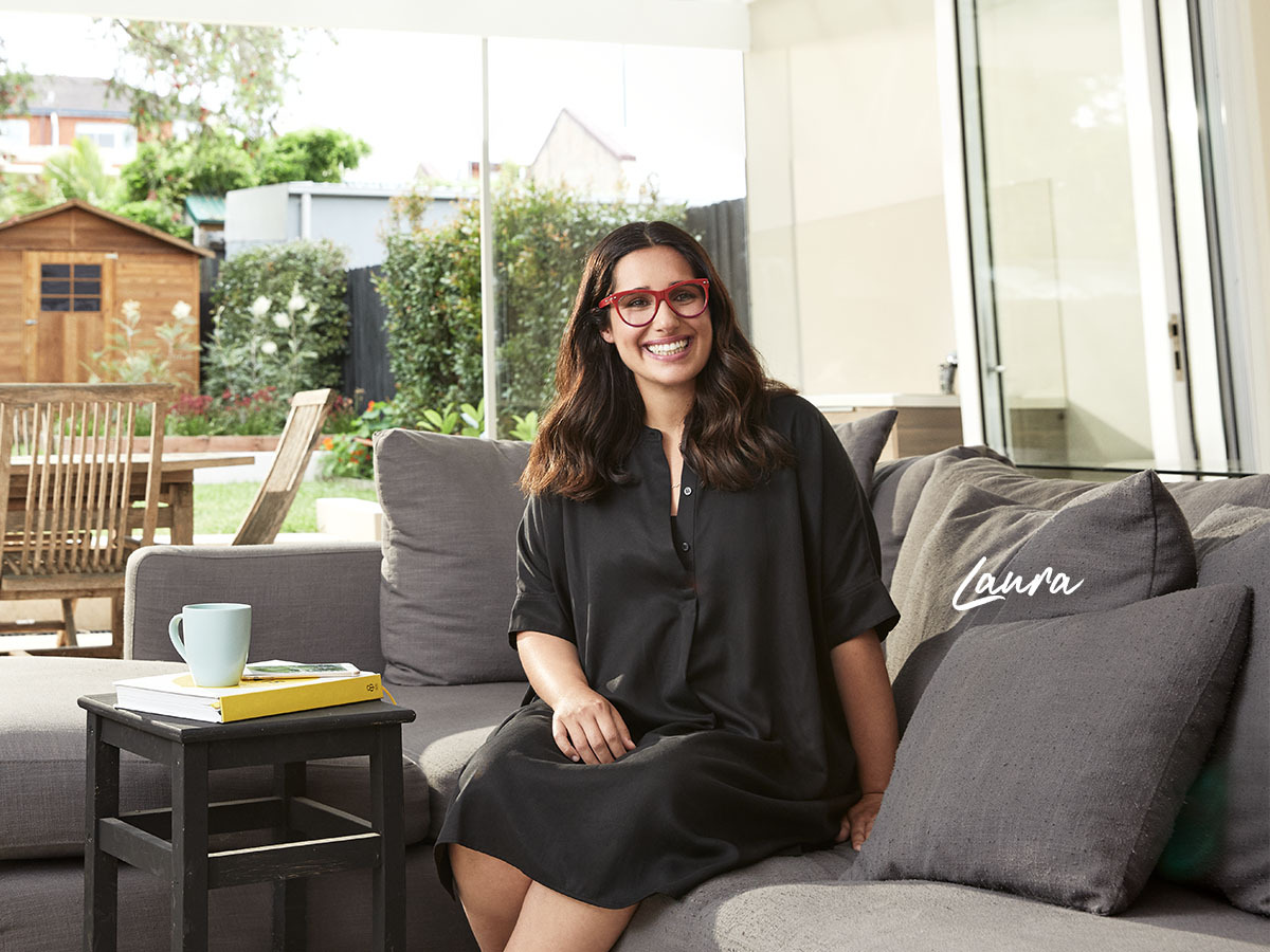 Laura Bates home loan customer with red glasses sitting on couch in house smiling