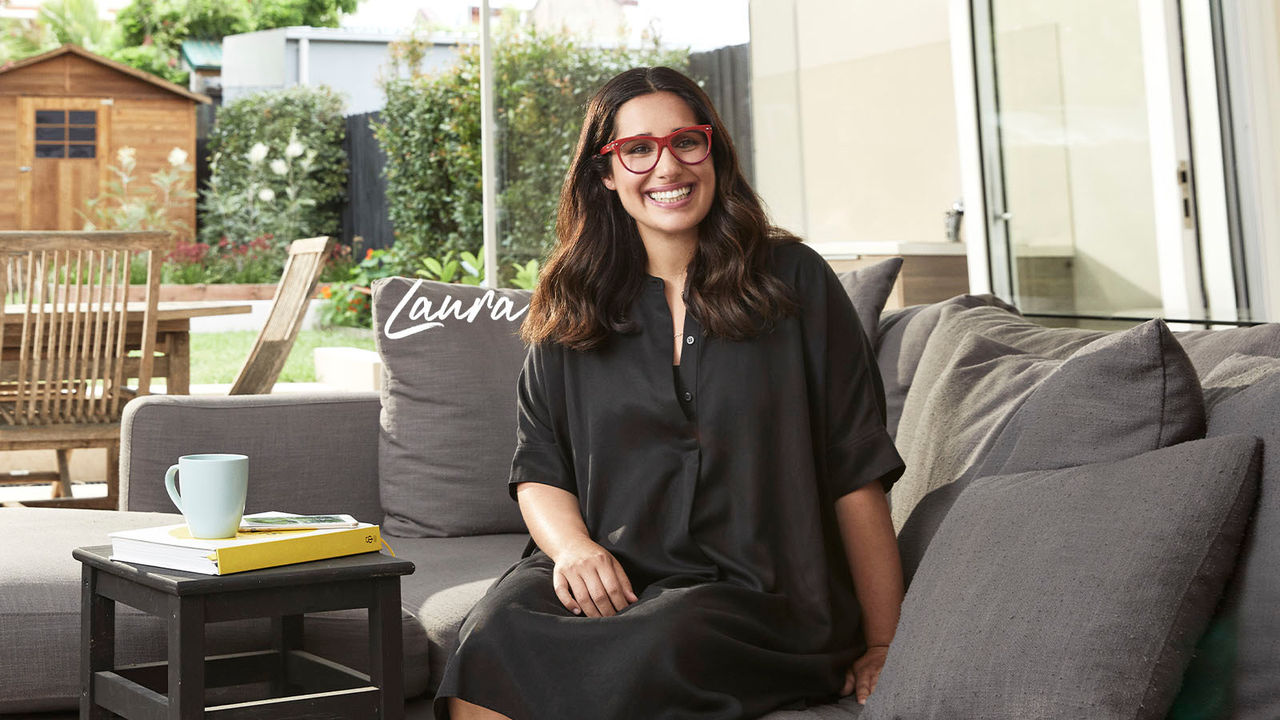 Laura Bates home loan customer with red glasses sitting on couch in house smiling