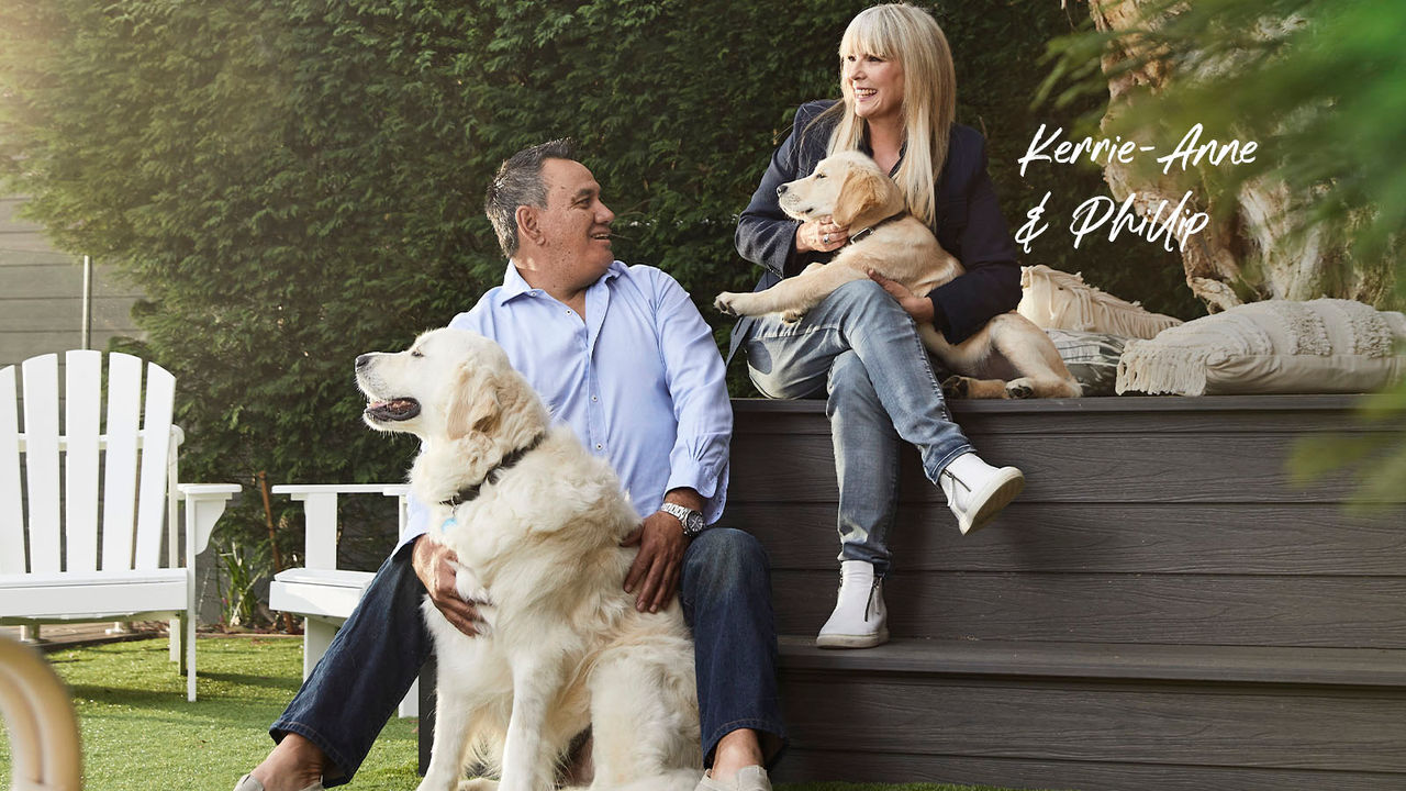 Kerrie-Anne and Phillip home loan customers smiling and sitting with two dogs in backyard