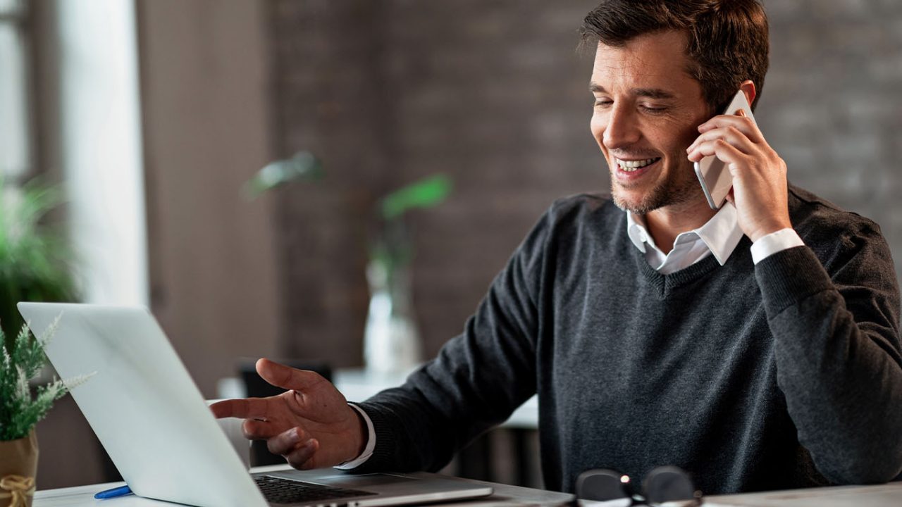 Happy businessman communicating over mobile phone and working on laptop while being at work.