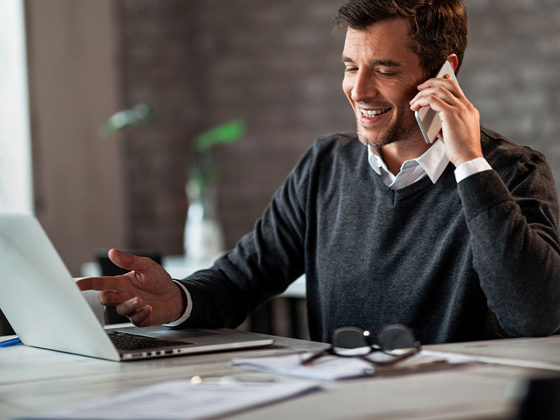 Happy businessman communicating over mobile phone and working on laptop while being at work.