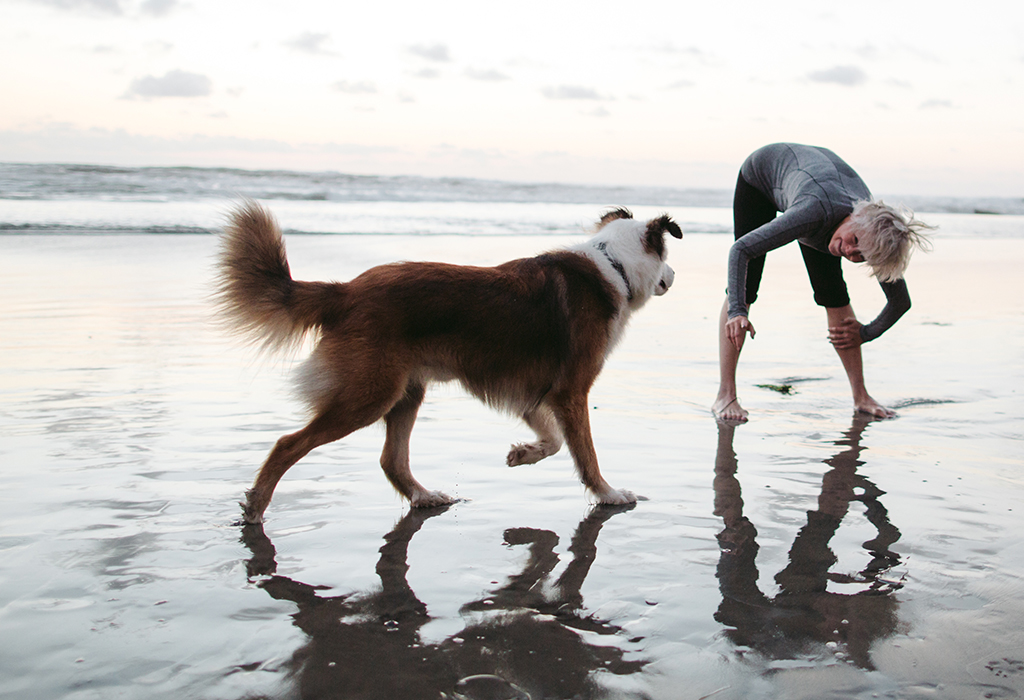 Mature woman playing with dog on beach at sunset