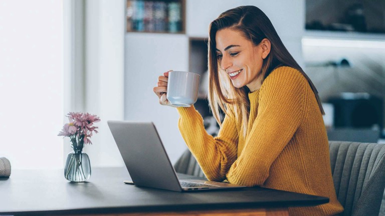 woman looking at computer with coffee cup smiling